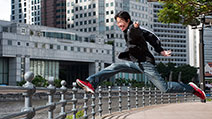Photograph of a photographer striding over railings, and taking the picture using a remote control.