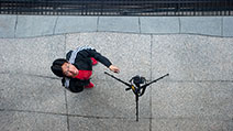 Photograph of a top-down reflection of a photographer triggering a camera on a tripod using a remote control.